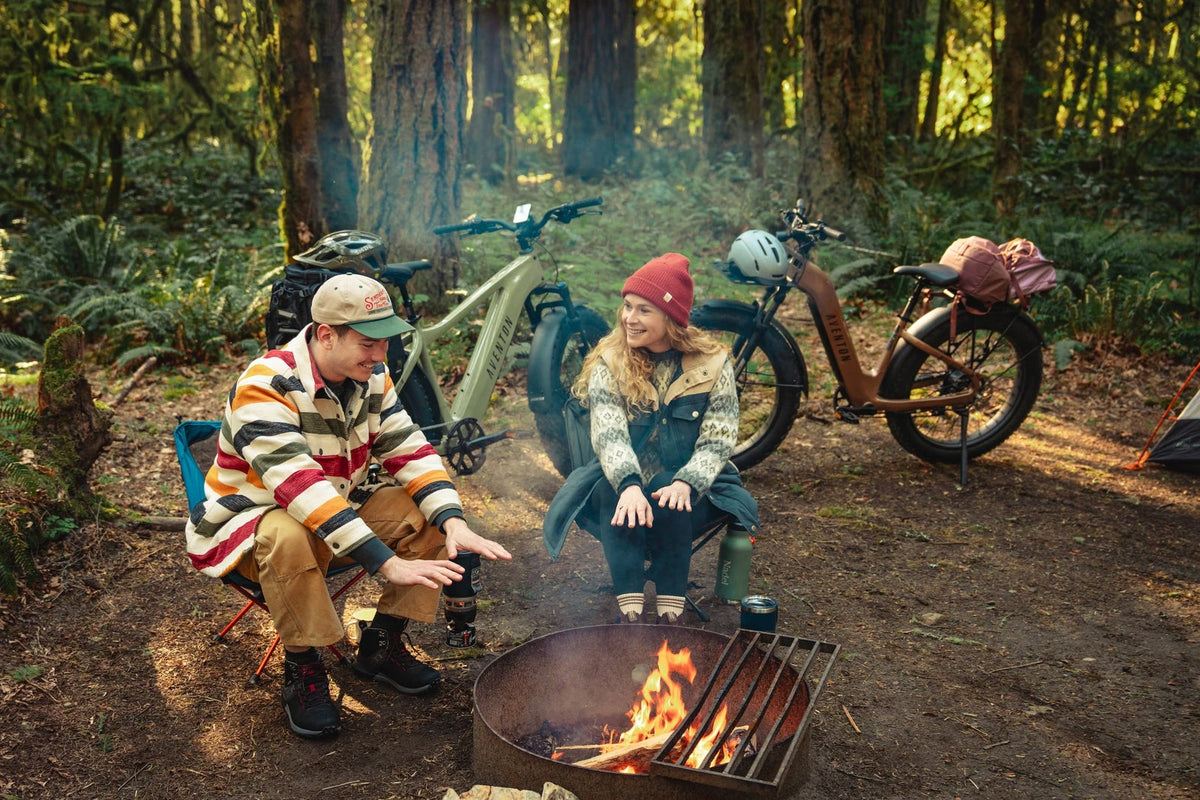 Two riders by a campfire with their Aventon Aventure 3 e-bikes